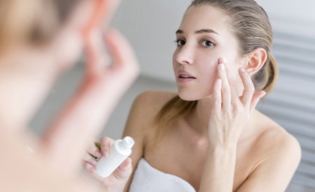 Woman applying cream on her face in a bathroom