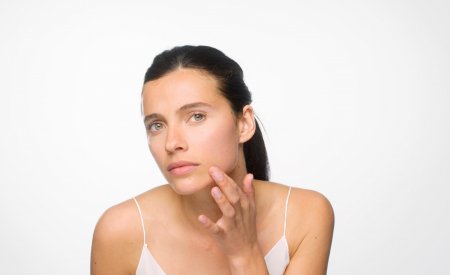 A woman examining her skin in the mirror as part of her clear skin routine