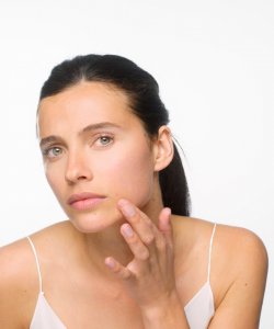 A woman examining her skin in the mirror as part of her clear skin routine